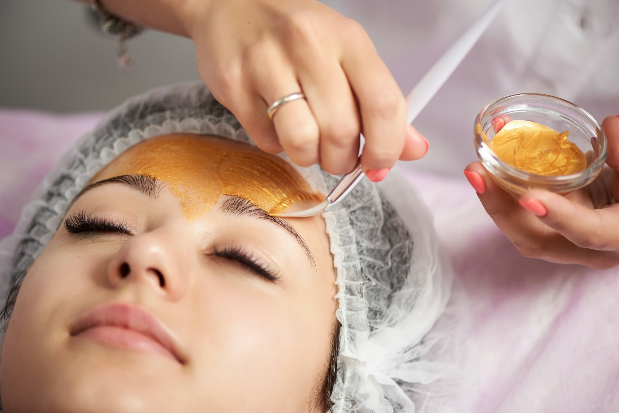 Close-up of portrait of beautiful girl in a special hat on her head applying gold facial mask.